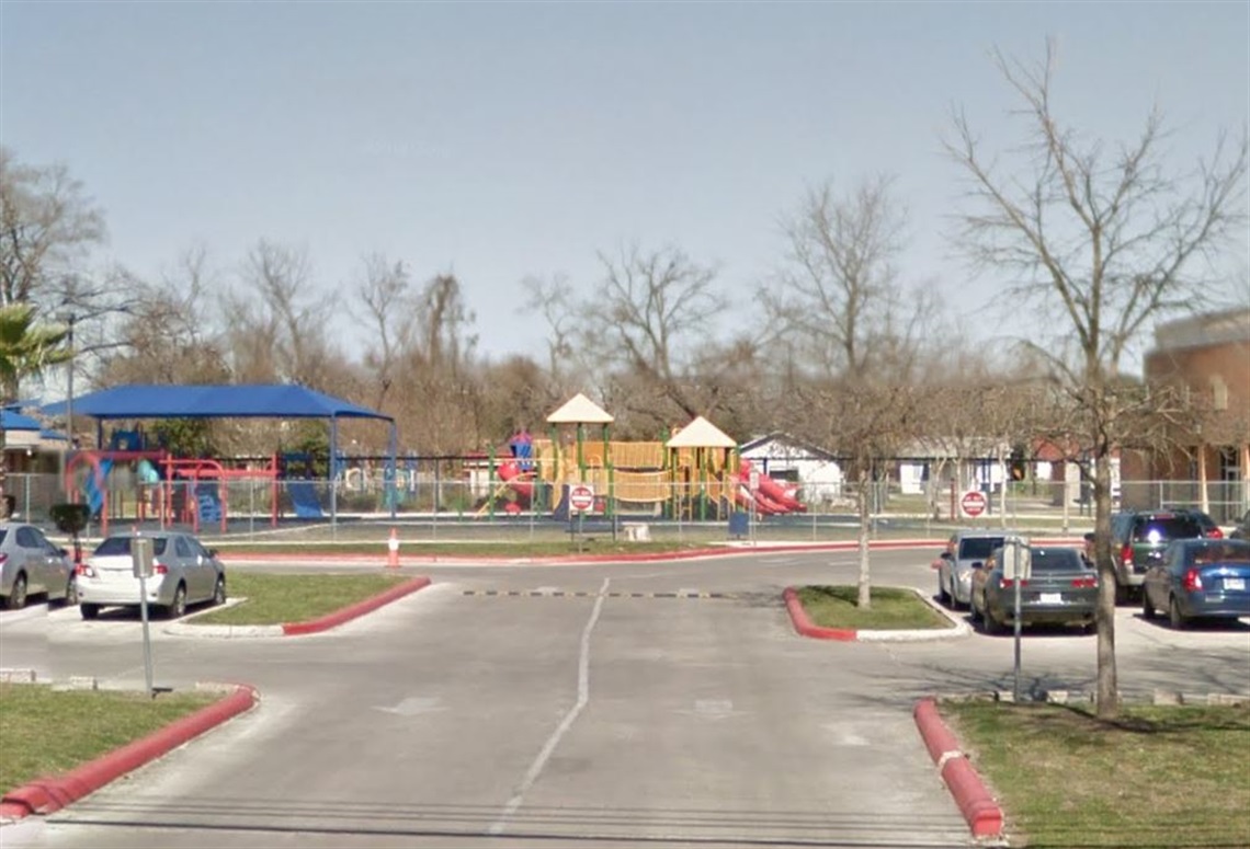 A parking lot filled with parked cars adjacent to a colorful playground area.