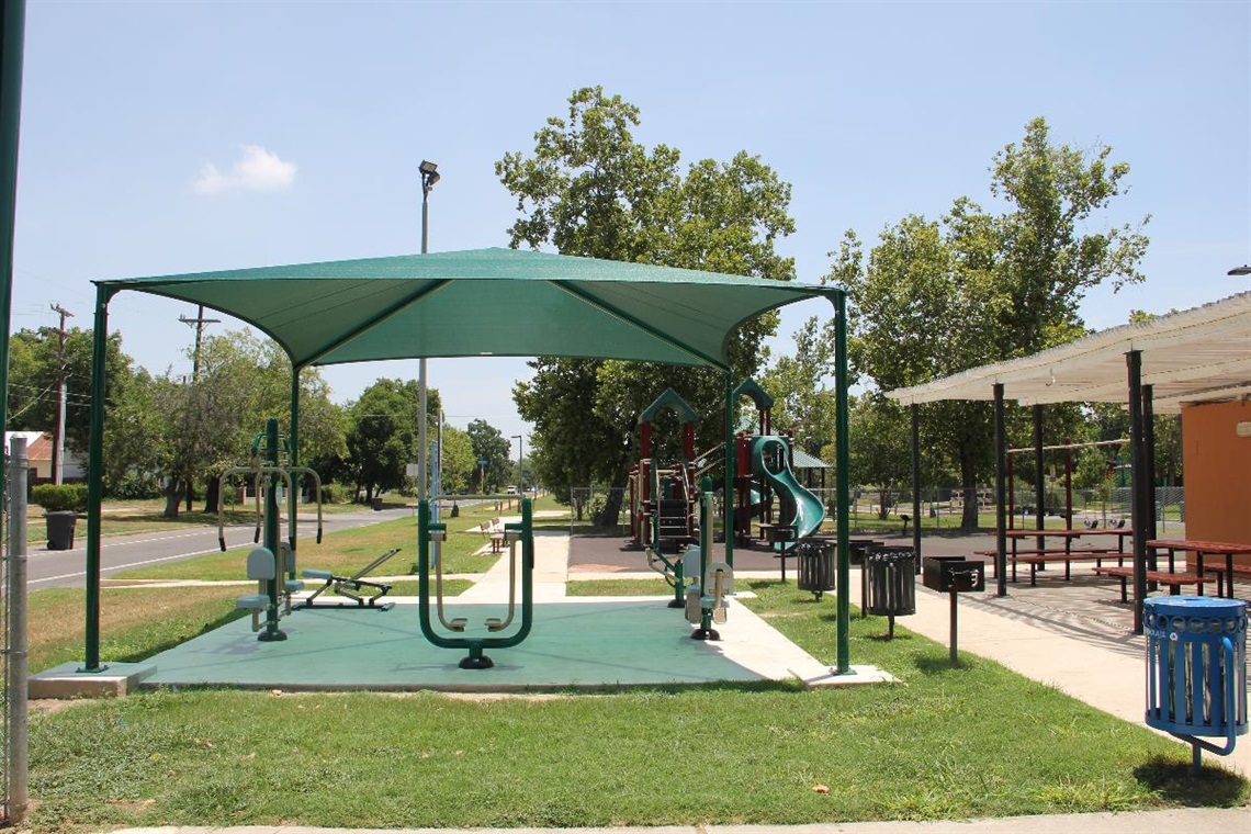 Fitness stations in the foreground can be used as an outdoor gym. There is a playground with slides in the background.