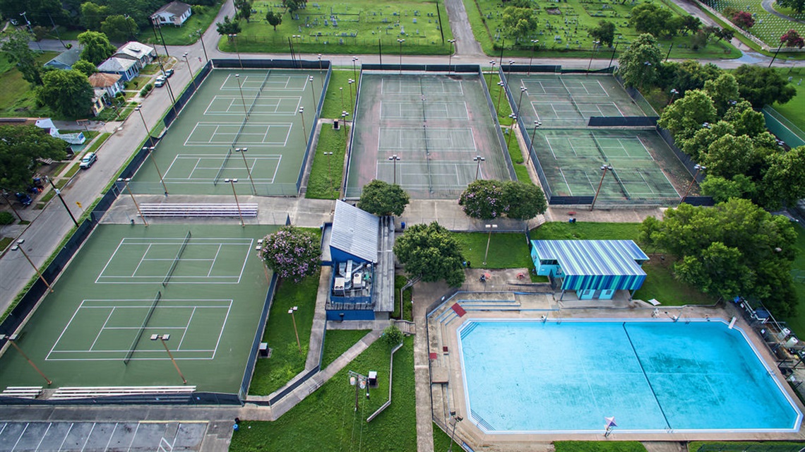 Aerial view of Fairchild park showcasing tennis courts adjacent to a swimming pool, highlighting the vibrant green courts and blue water.