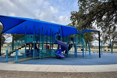 Playground with a slide and climbing structures covered by a blue shade structure.