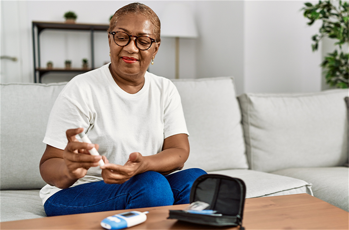 Woman checking blood sugar with glucose monitor while sitting on a couch at home.