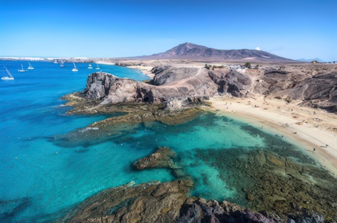 Aerial image of Playa Blanca, white sand beach with volcanic cliff in Lanzarote, Canary Islands, Spain.