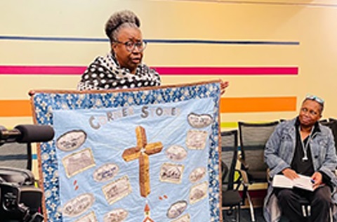 Woman holding quilt with the word Cornerstones.