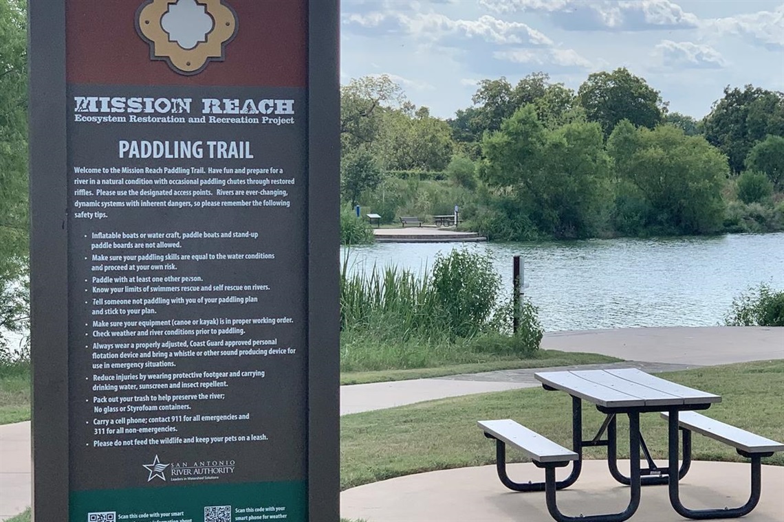Acequia park in San Antonio, a park table with a park sign and a pond in the background.