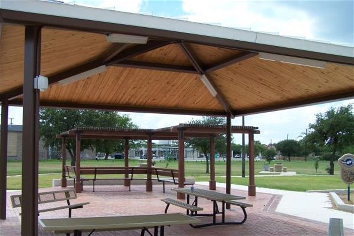 Shaded picnic tables and benches are arranged under a pavilion.