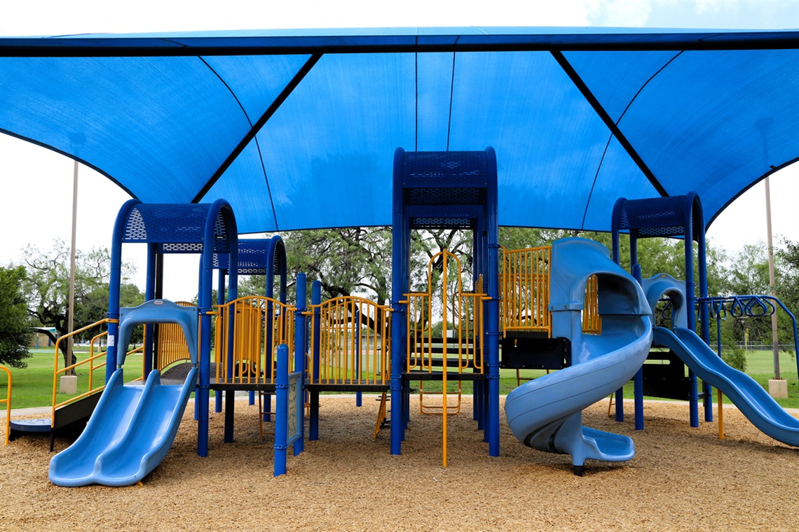Blue and yellow playground with slides under a large blue shade canopy.