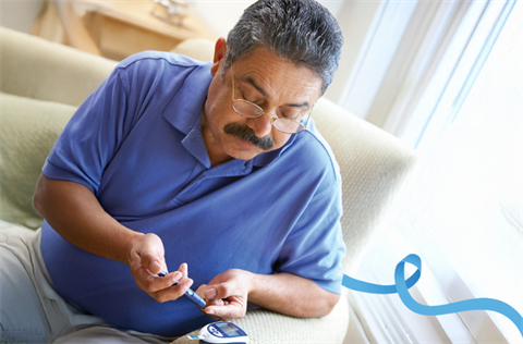 Man sitting on a couch using a glucose meter to check his blood sugar level.