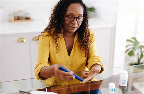 Woman sitting at a glass table using a glucose meter to check her blood sugar level.